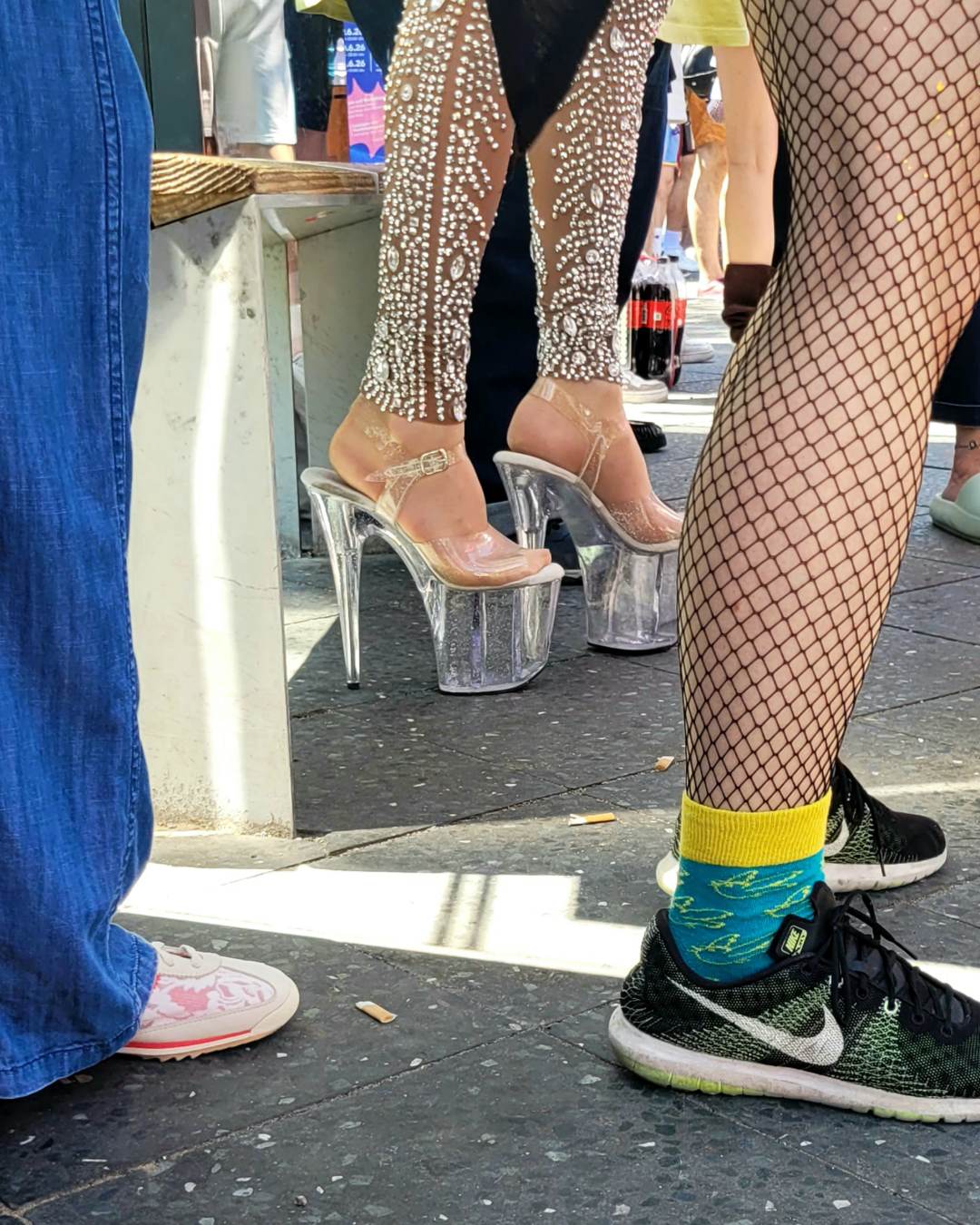 Straßenszene mit Beinen in Fischnetzstrumpfhose, bunten Socken und hohen transparenten Plateauschuhen.